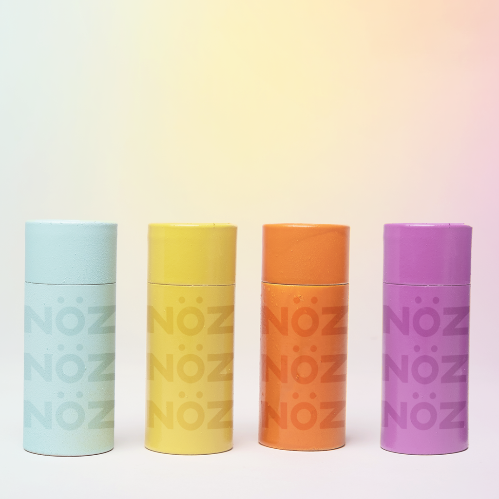 Nöz blue, yellow, orange and purple sunscreen presented side by side in a straight line on a gradient background.