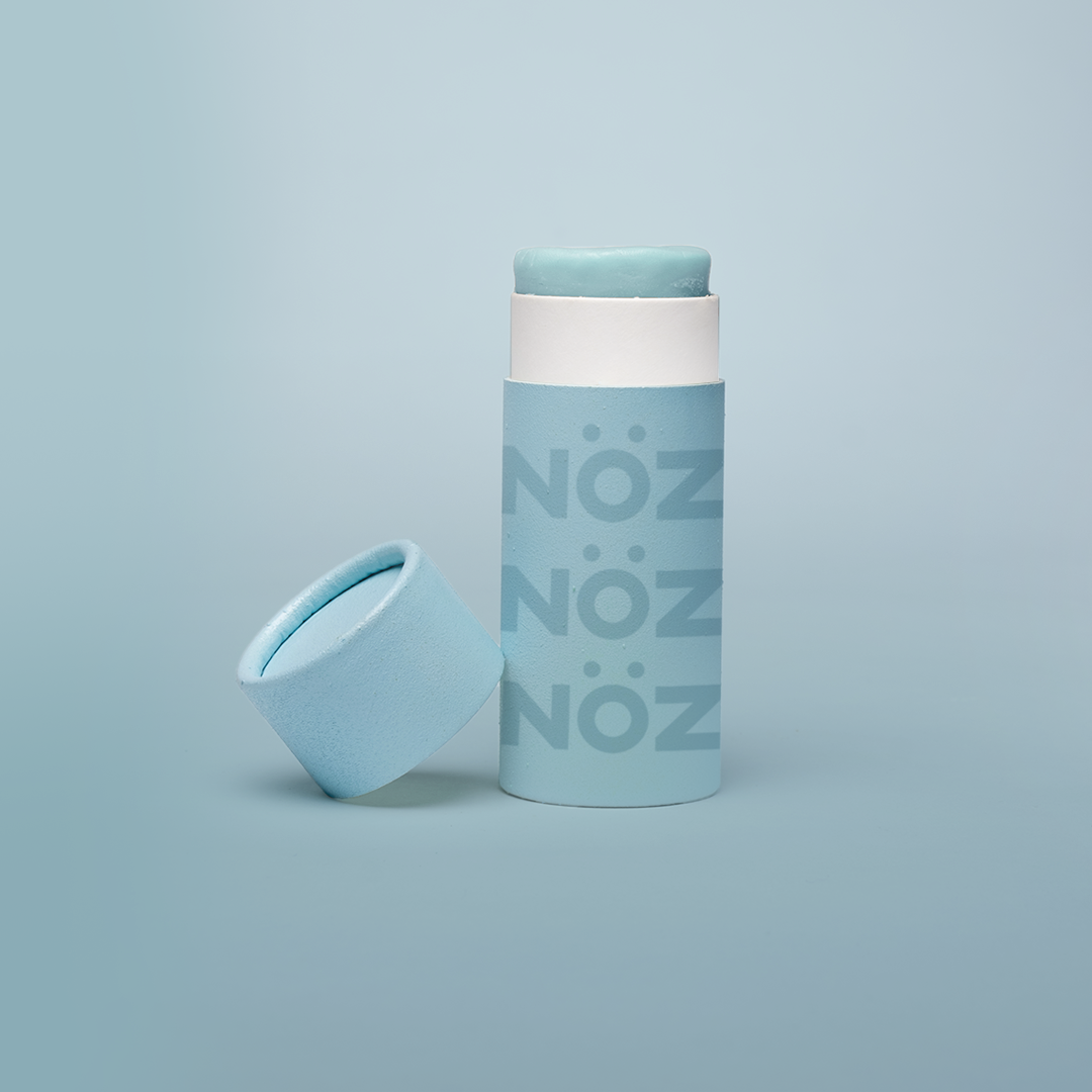  An open tube of blue Nöz sunscreen with its lid tilted beside it and shown against a blue background