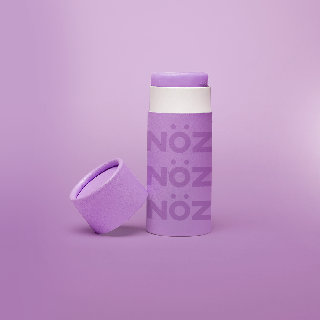 An open tube of purple Nöz sunscreen with its lid tilted beside it and shown against a purple background