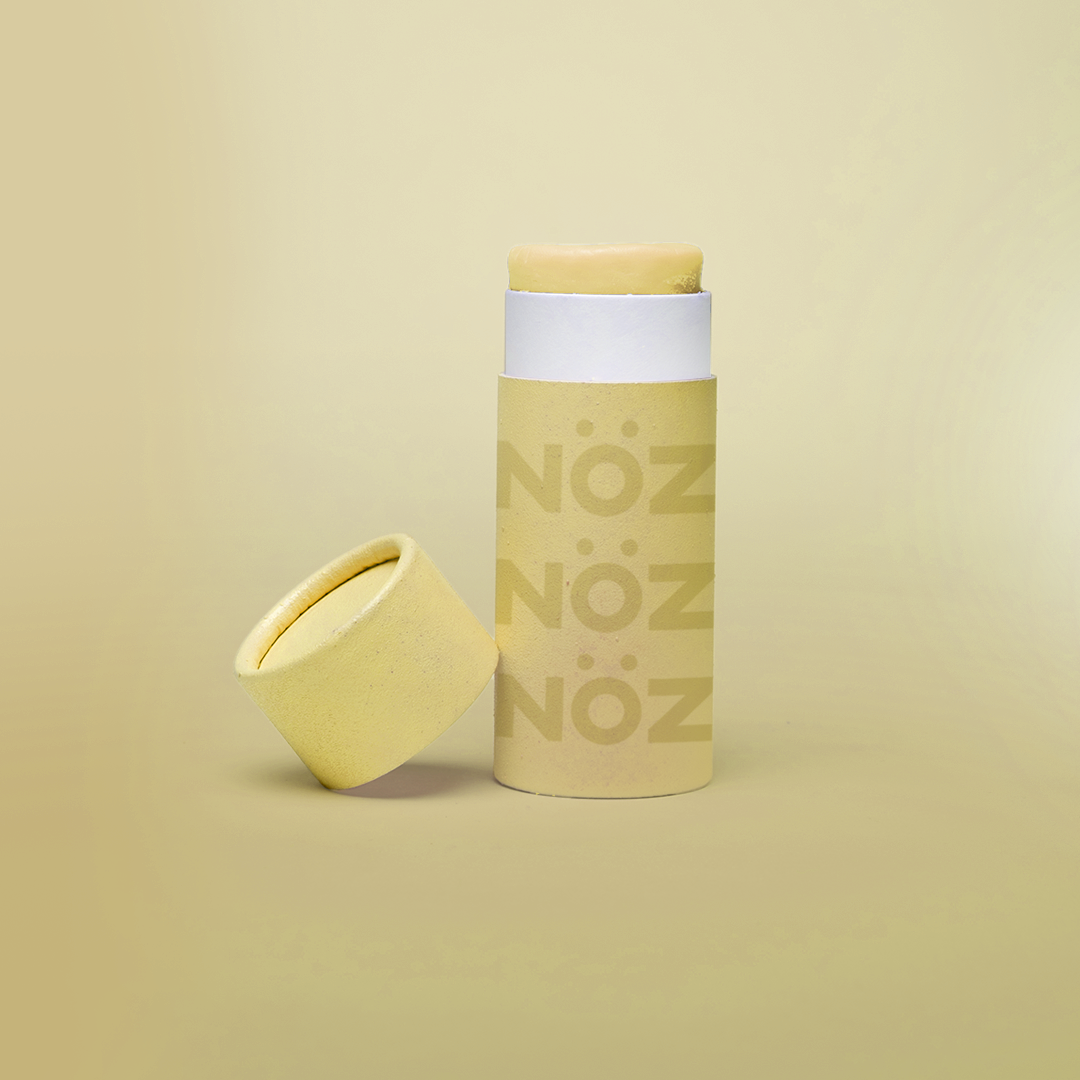 An open tube of yellow Nöz sunscreen with its lid tilted beside it and shown against a yellow background